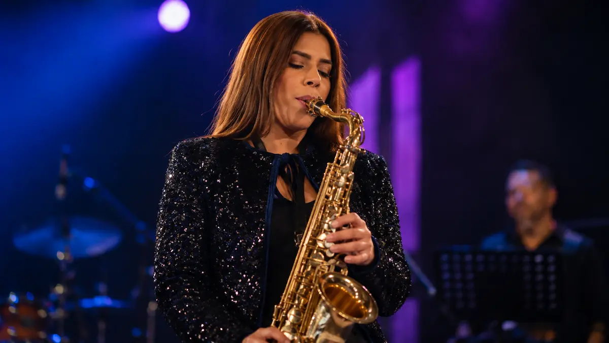Ilustración editorial de saxofonista tocando en escenario con luces violetas y músicos desenfocados al fondo